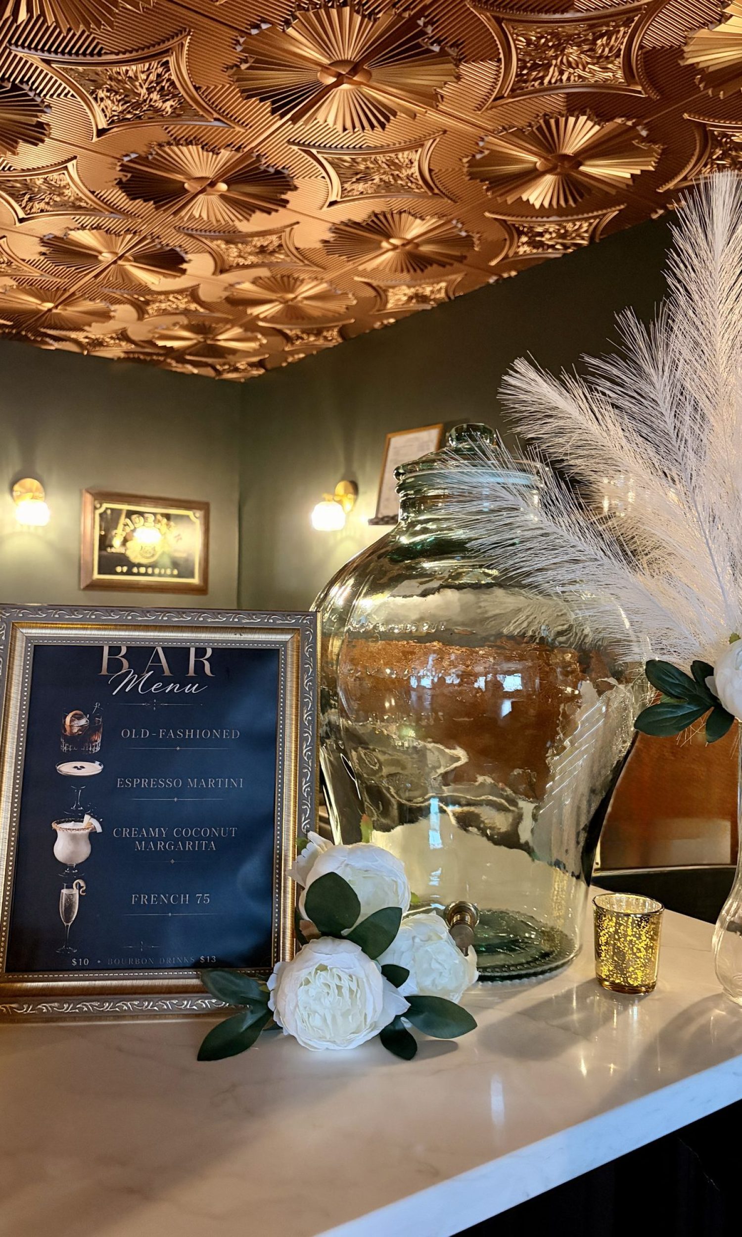 Framed bar menu with cocktail list beside gold ceiling tiles at The Event Vault