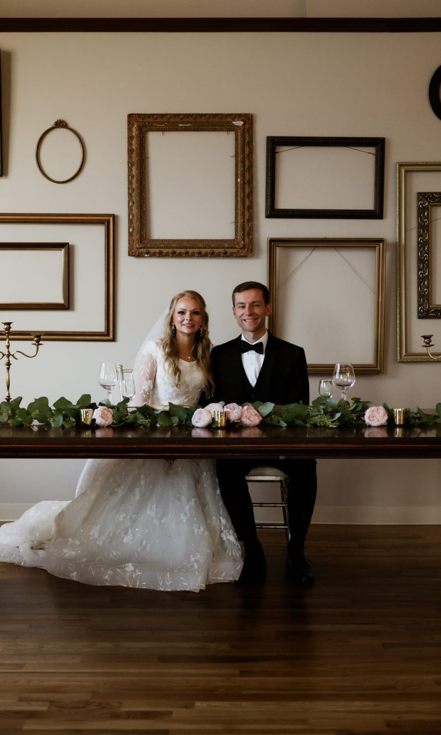 Bride and groom seated at the head table before The Event Vault gallery frame wall